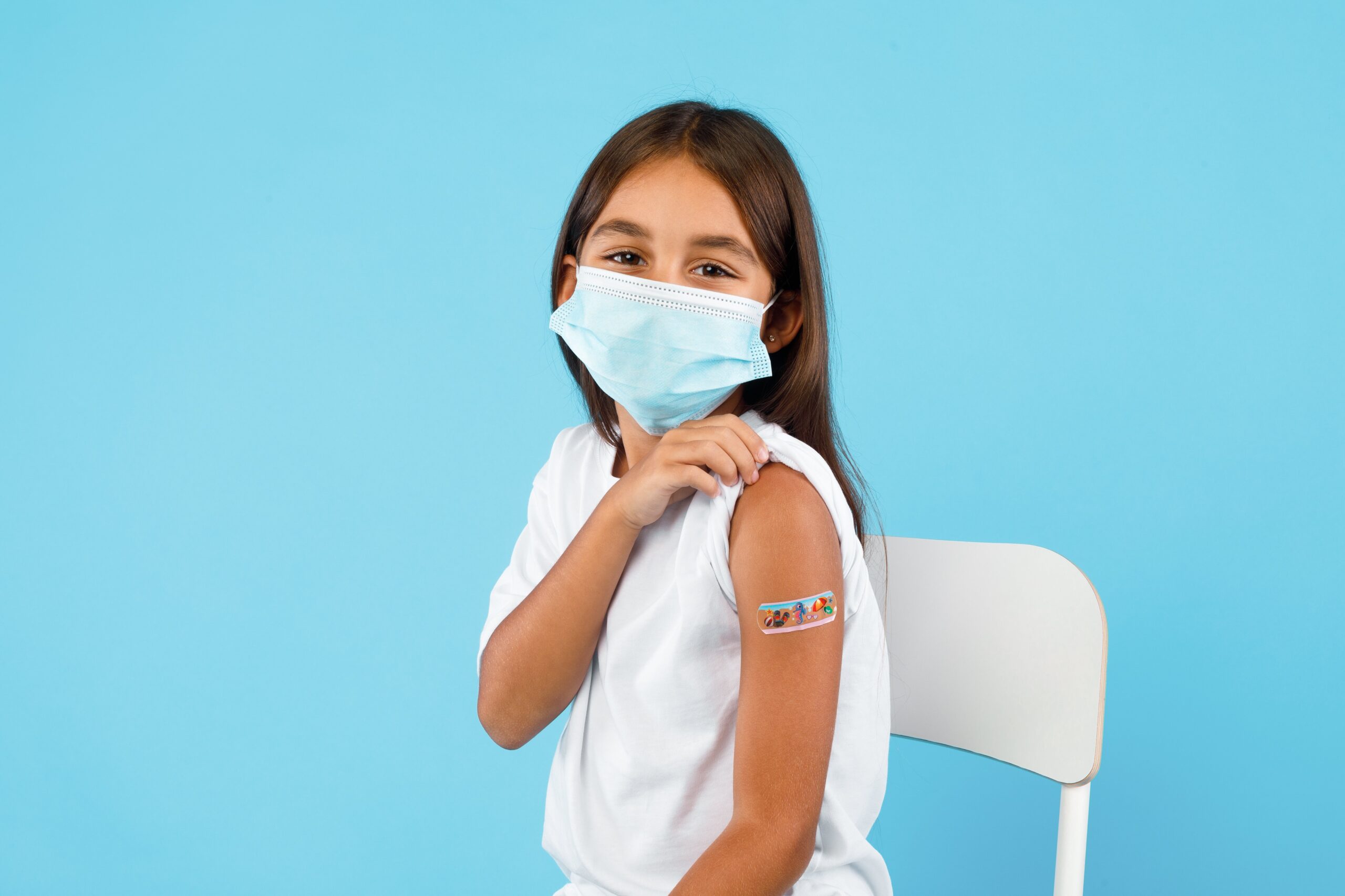 A child sitting on a chair with a band aid on her arm.